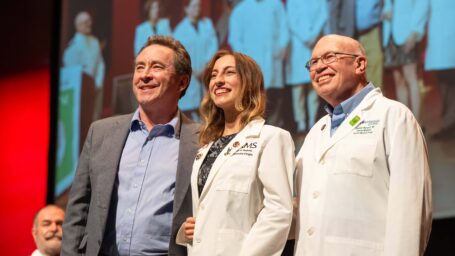 A medical student a white coat ceremony standing on stage with two men