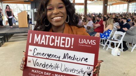 A senior holds a sign showing where she matched for residency