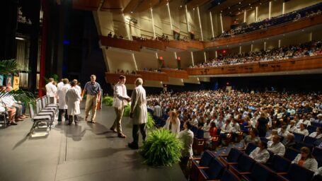 White Coat Ceremony. A faculty member shakes a student’s hand in a large auditorium
