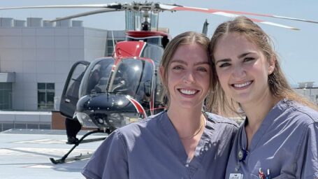 Two female medical students pose in front of a helicopter